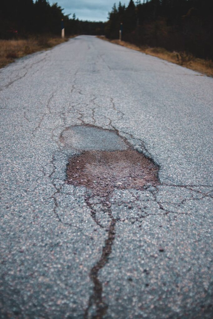 empty asphalt road with cracks going between coniferous trees on cloudy day